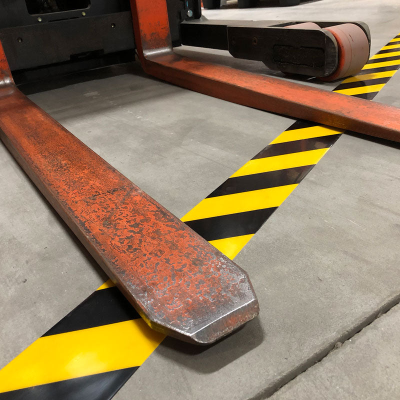 AS450 Yellow/Black ArmorStripe™ Hazard Stripe High Traffic Ultra-Durable Heavy Duty Warehouse Adhesive Floor Marking Tape (100 ft) in the path of a forklift