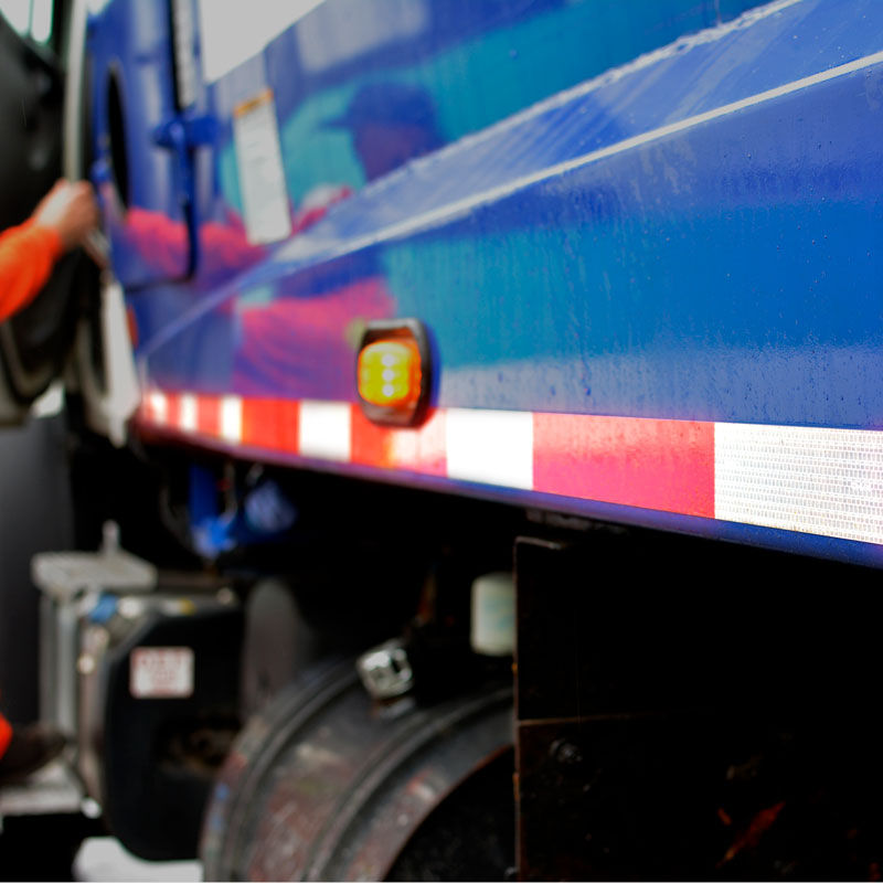 V57203 DOT Conspicuity Adhesive Reflective Trailer Tape (7in /11 in white/red pattern) 2 in x 150 ft applied to the side of a Garbage Truck