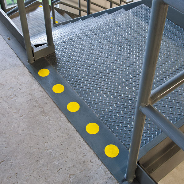 VC300Y Yellow Warehouse Floor and Lane Marking 3 inch Adhesive Circle Shapes (100/roll) applied to the top of a staircase for visual warning