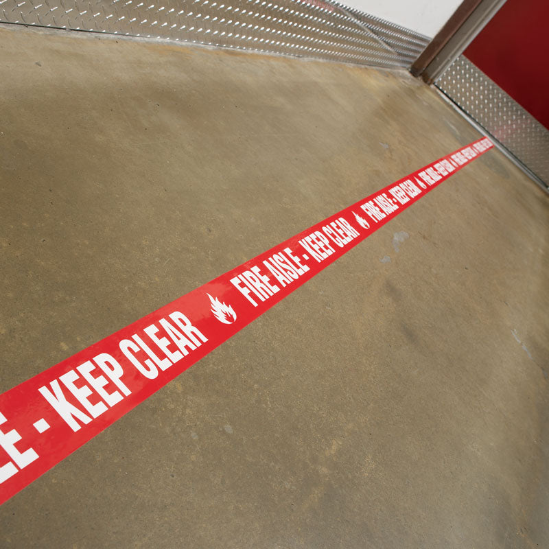 WTP105 FIRE AISLE - KEEP CLEAR White on Red Printed Safety Message Warehouse Floor Marking Tape (3 in x 54 ft) applied to a warehouse floor to mark a Fire Aisle